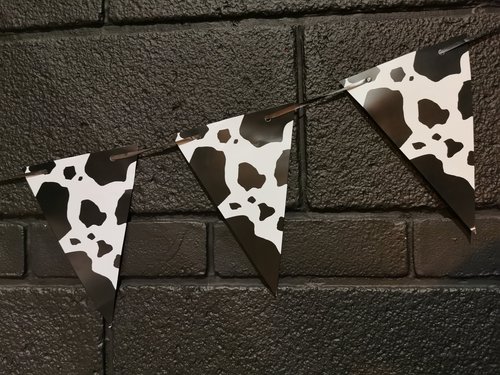 Three pieces of bunting hang across a black wall. The bunting is a black and white cow print.